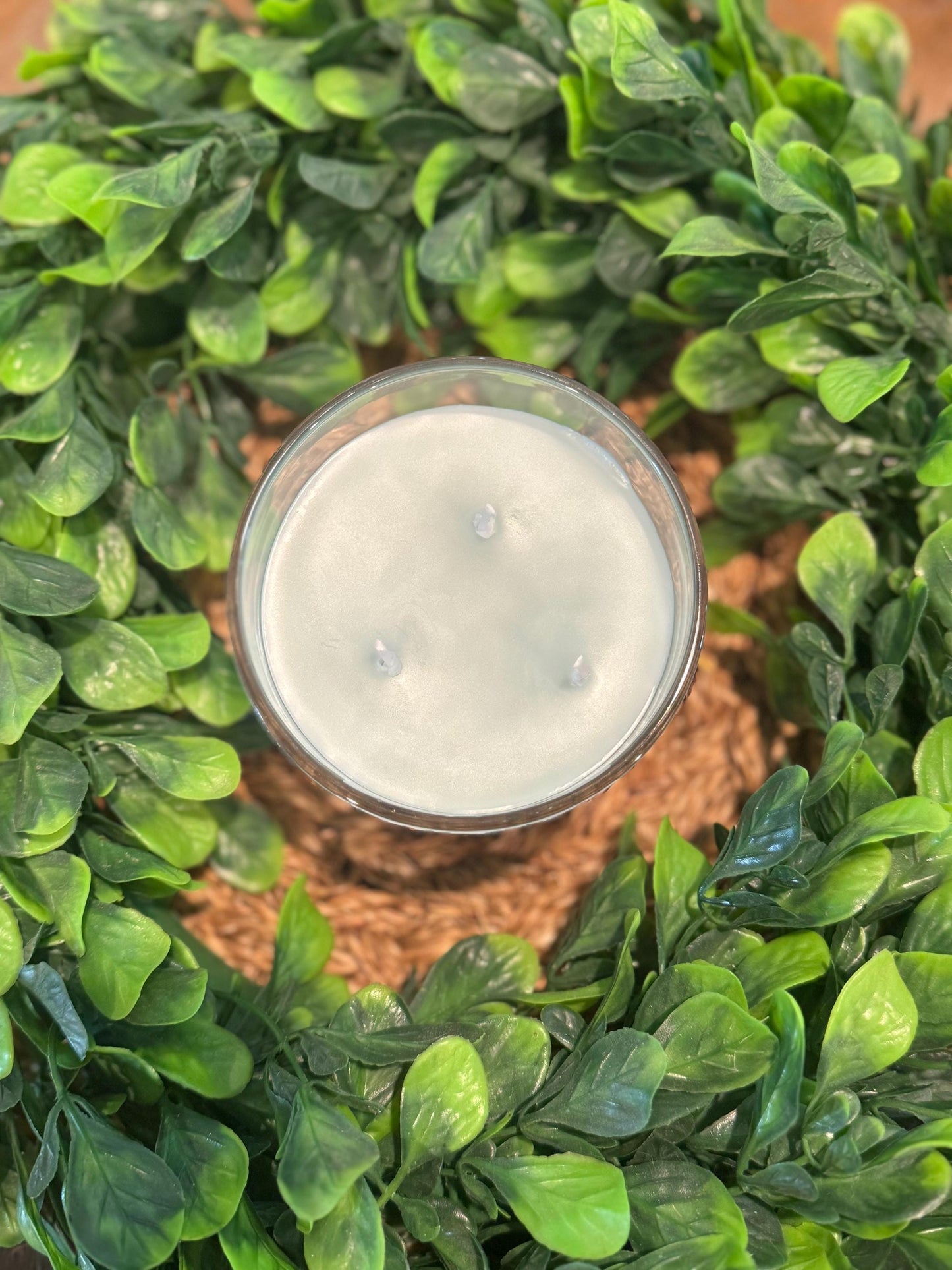 a candle in a glass surrounded by green leaves